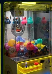 Crane machine with a claw poised over prize capsules