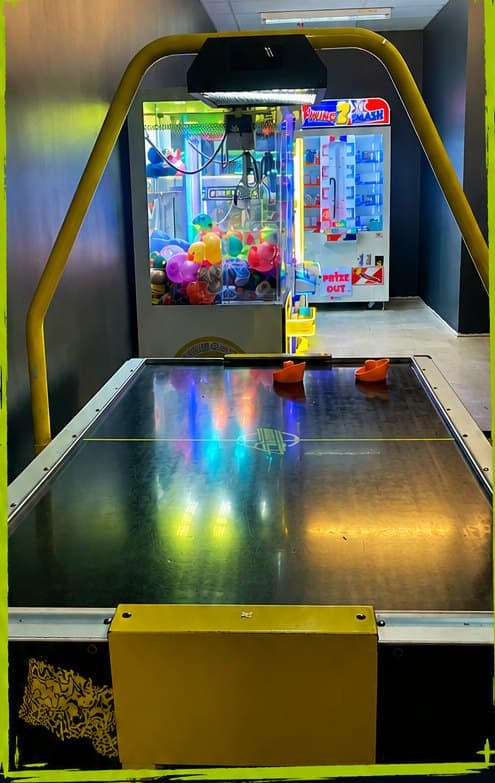 A lit air hockey table with claw machines behind it
