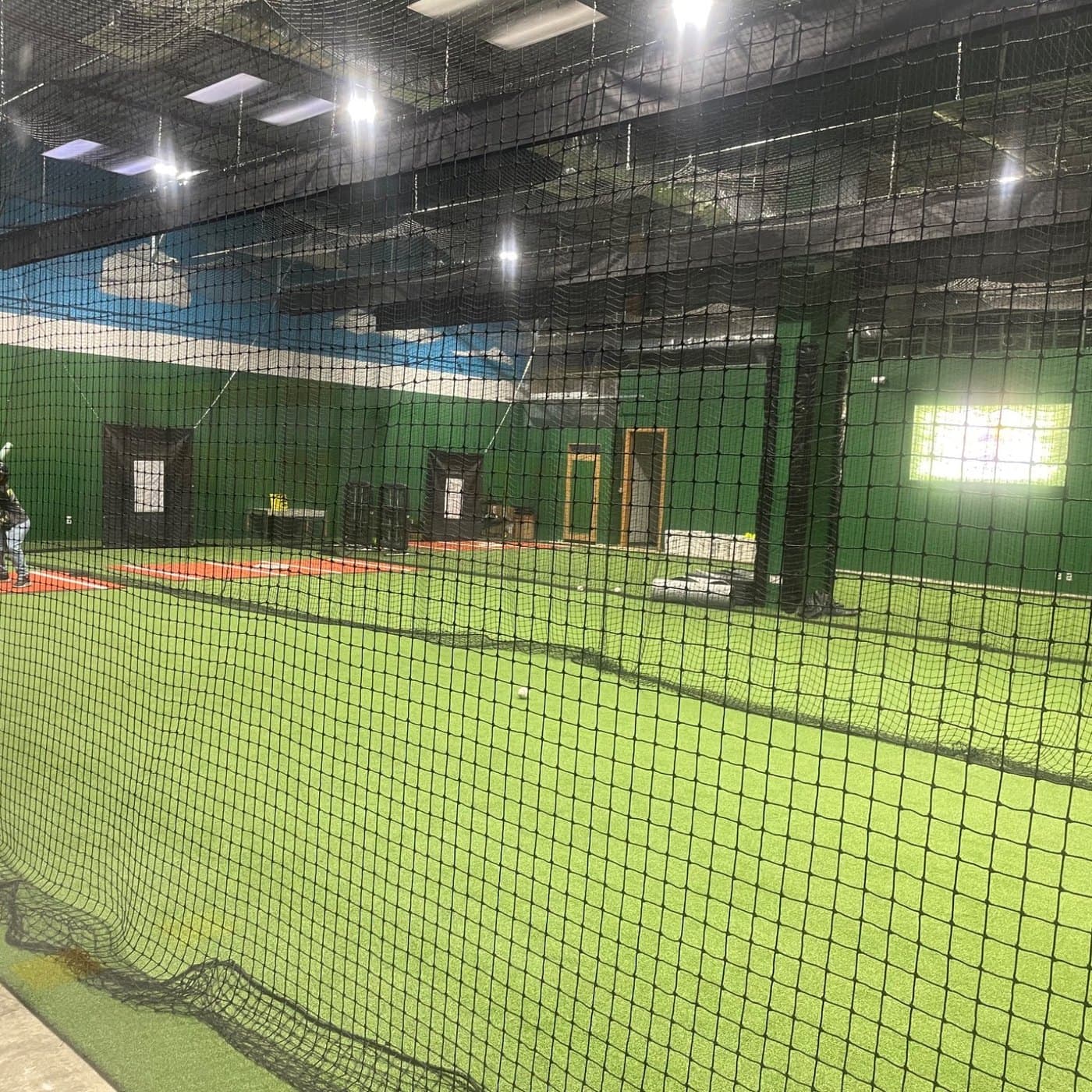 A wide view of the netted batting cage bays lit from overhead