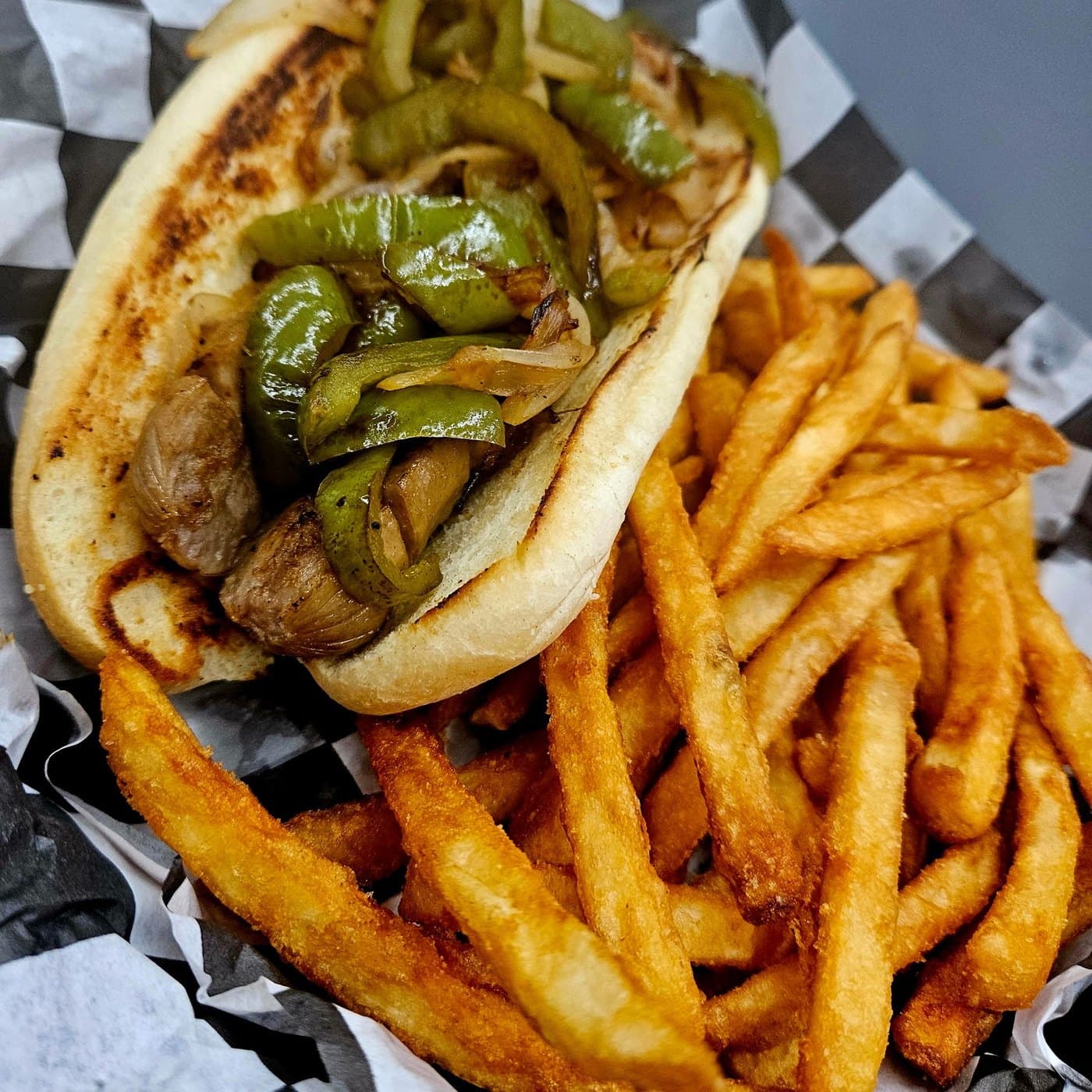 The Stadium Sausage: grilled sausage with peppers and onions on a bun, beside a basket of fries