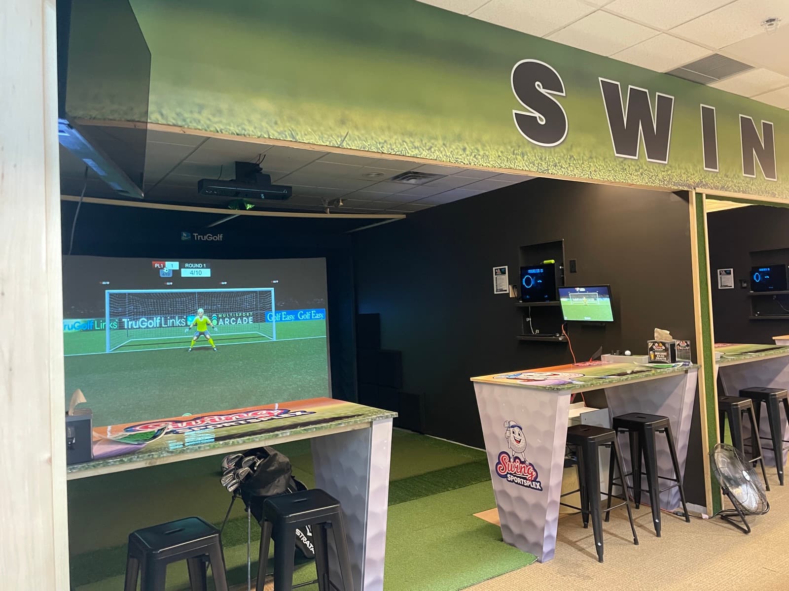 The simulator lounge under the SWING sign, with branded high-top tables and stools